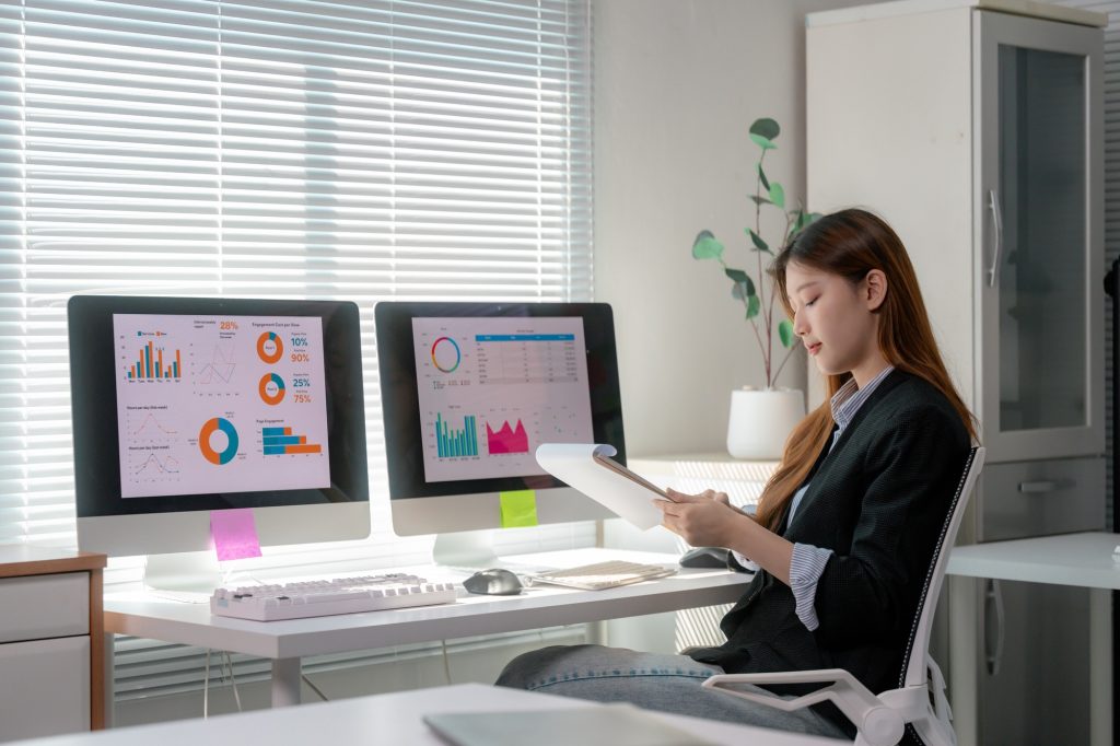 Businesswoman analyzing financial charts and graphs on computer screen and document