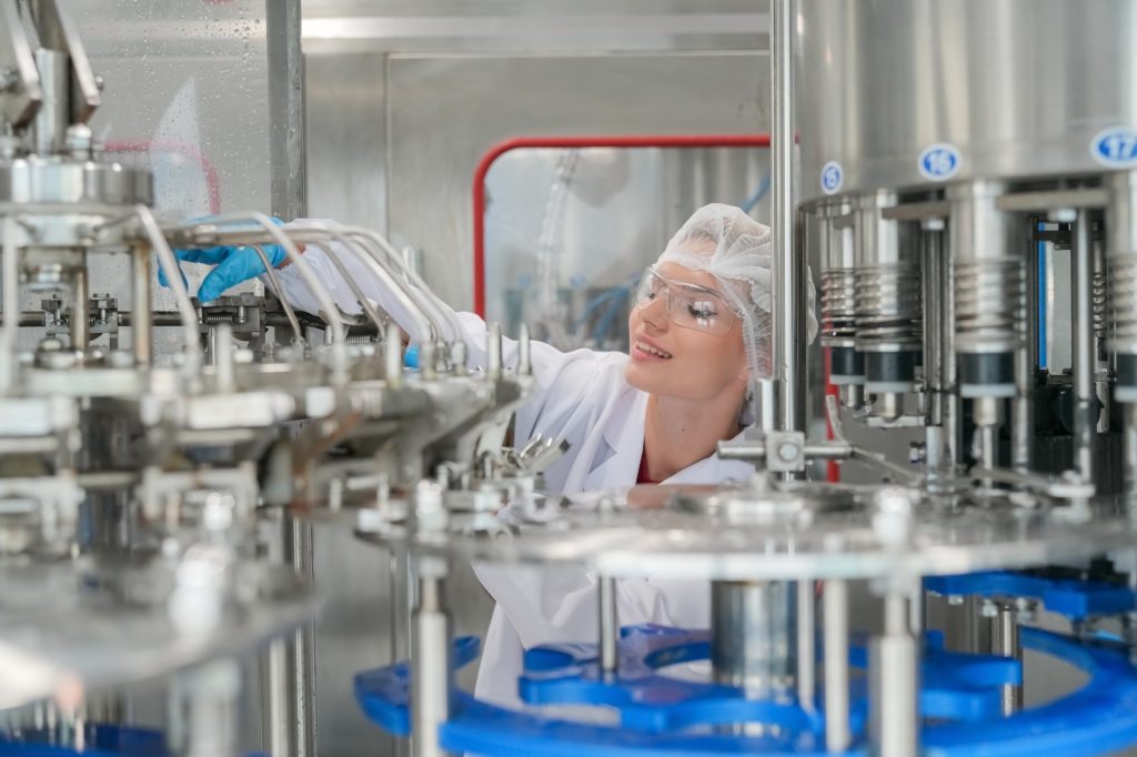 Female worker inspecting water bottle on production line in spring water factory