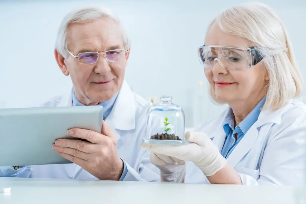 Smiling scientists with digital tablet and green plant in soil